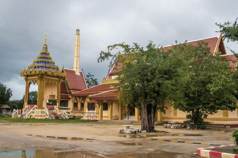 Very Thai photo: crematorium, temple, table under a tree, puddles and a speed bump on an earthen road.