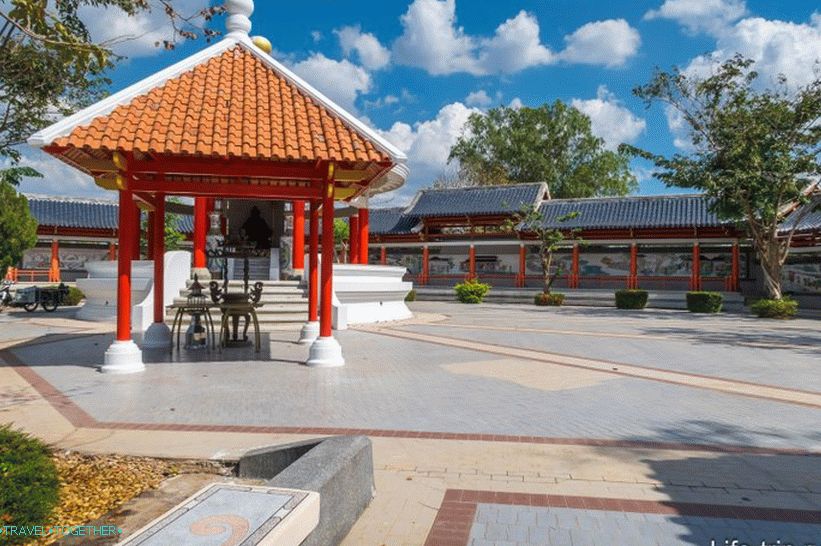 Sculpture of a Chinese deity under the roof and a wall along the park, with pictures on the tile