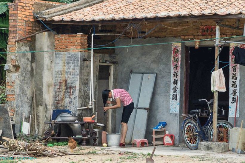 A girl washes her head in a bucket on the porch of her house